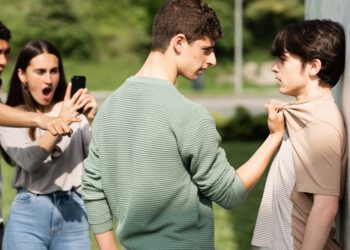 Teenager bully menacing boy while friends are recording. Bullying and violence at school concept